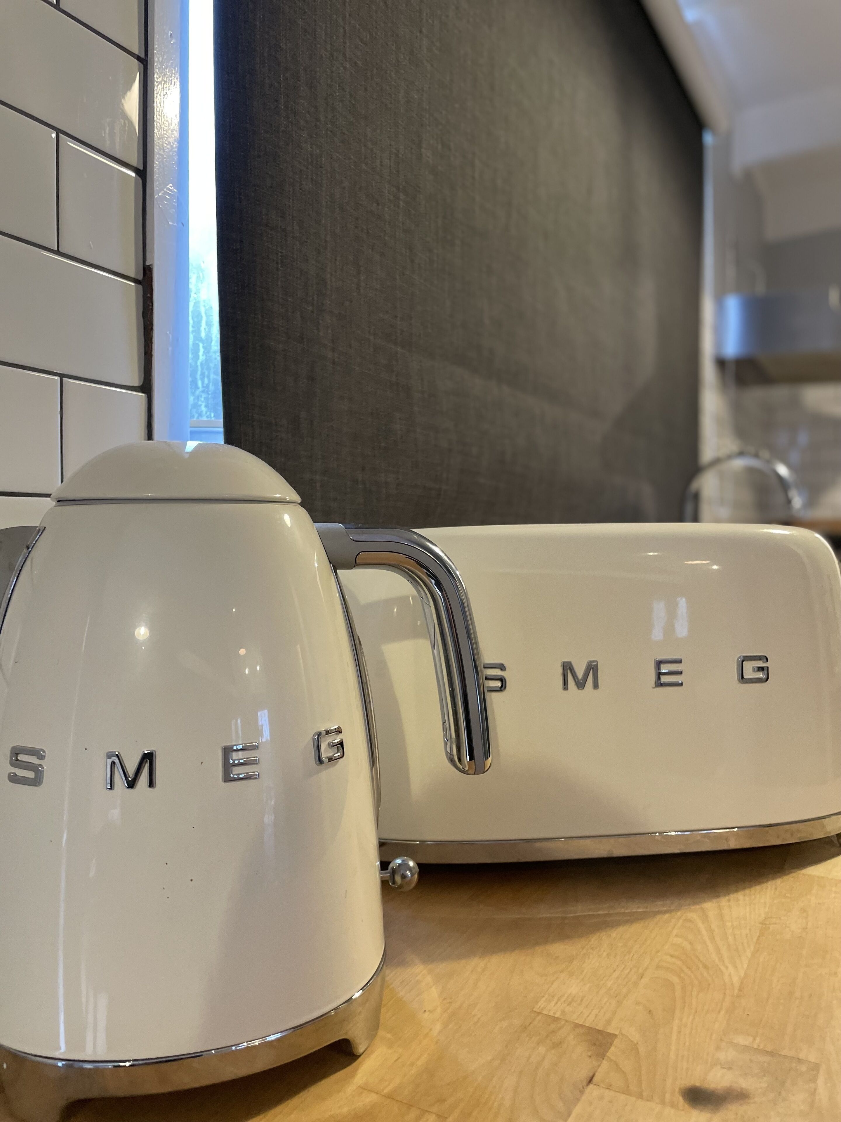 A kitchen with a white electric kettle and a white appliance with the brand name 'SMEG' on it.