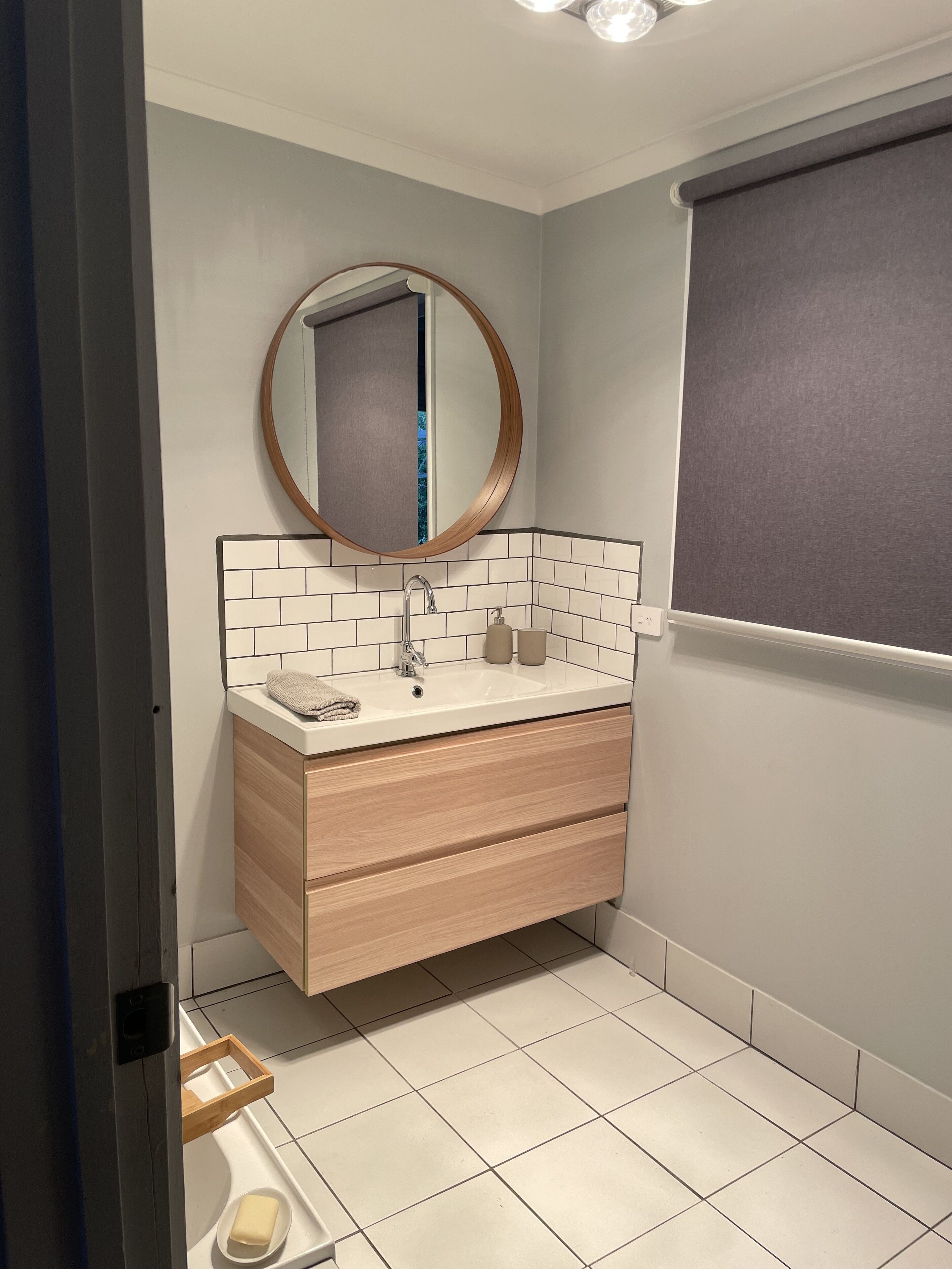Un baño moderno con un lavamanos blanco, tocador de madera y un espejo redondo.
