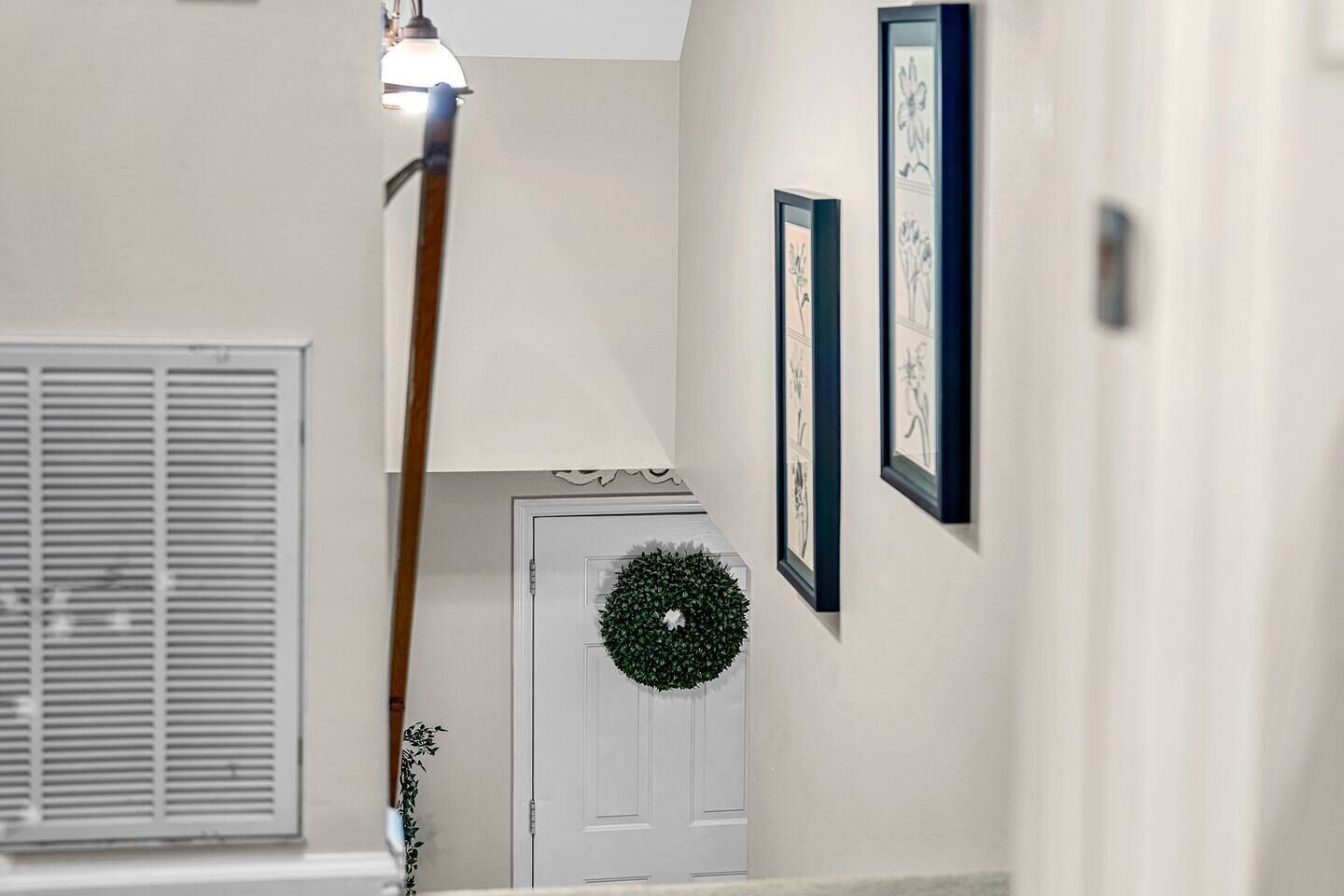 Un corridoio con una porta bianca, un'corona decorativa e quadri appesi al muro.