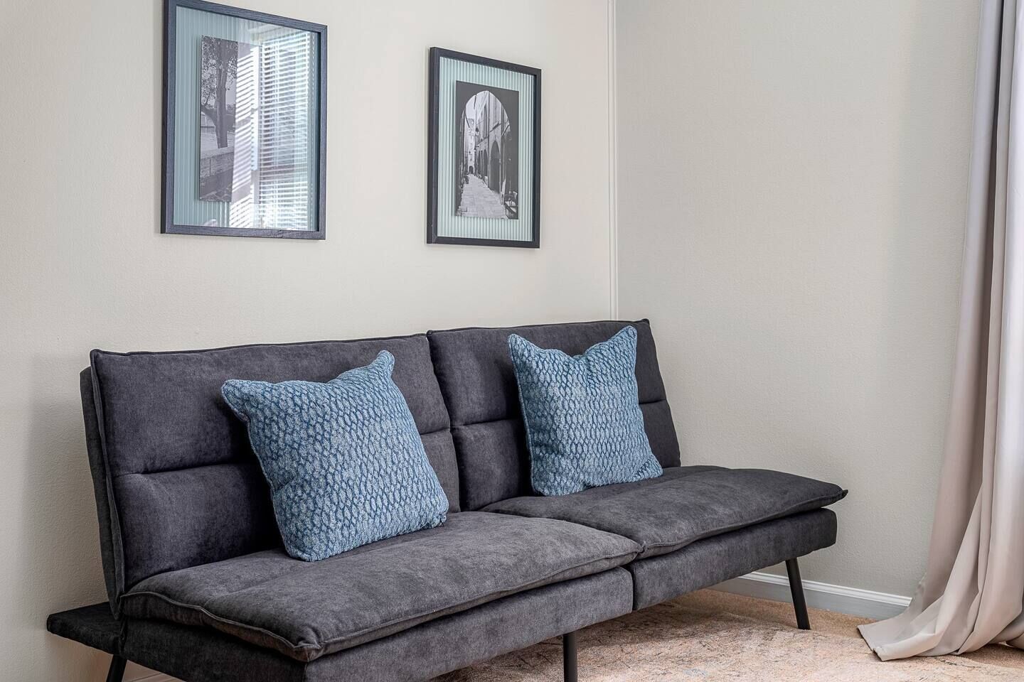 A grey sofa with two blue patterned cushions, positioned against a wall with two framed pictures above it.