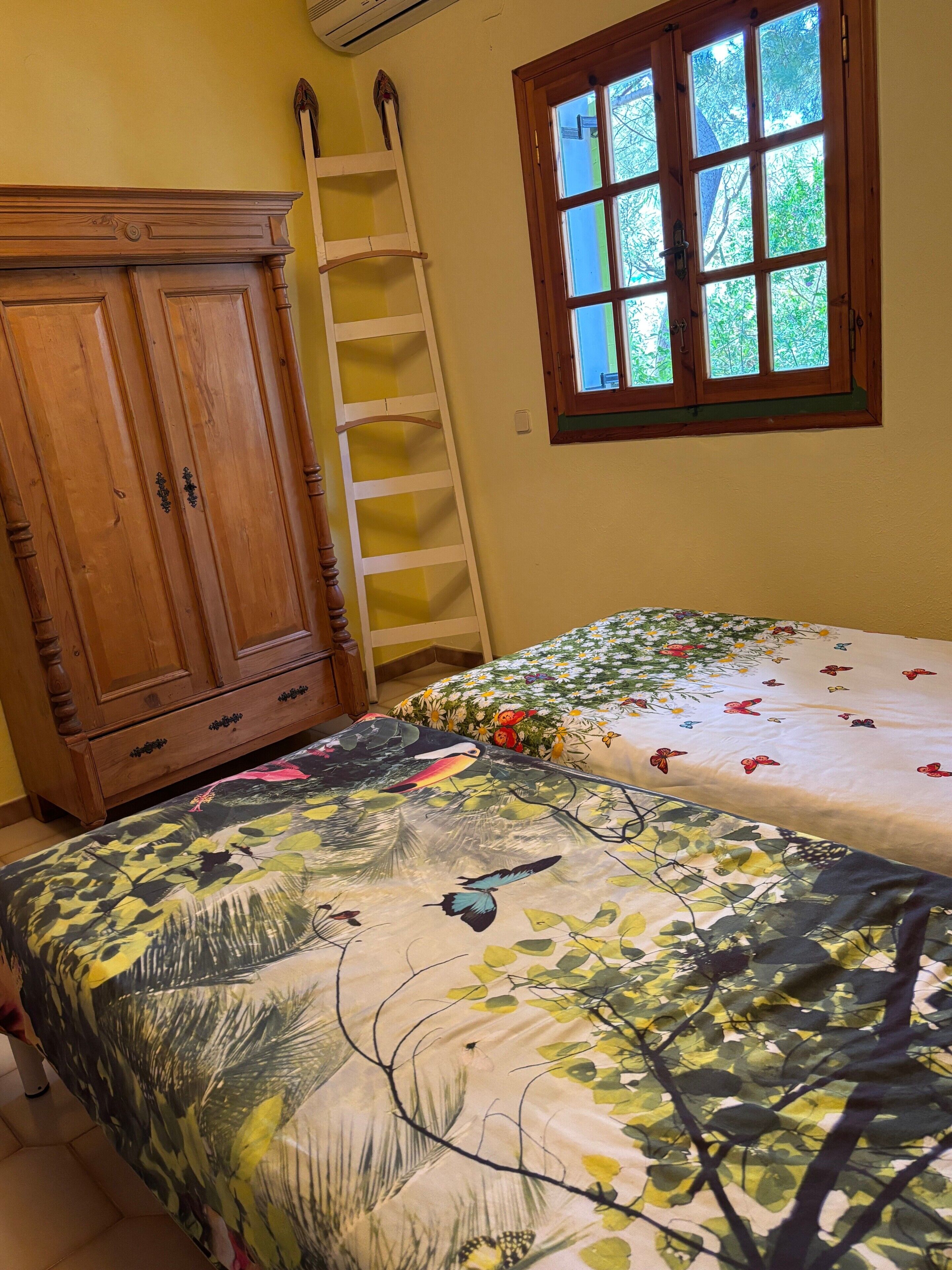 Una camera da letto con un'armadio in legno, una scala, un letto con biancheria da letto a fiori e una finestra vista alberi.