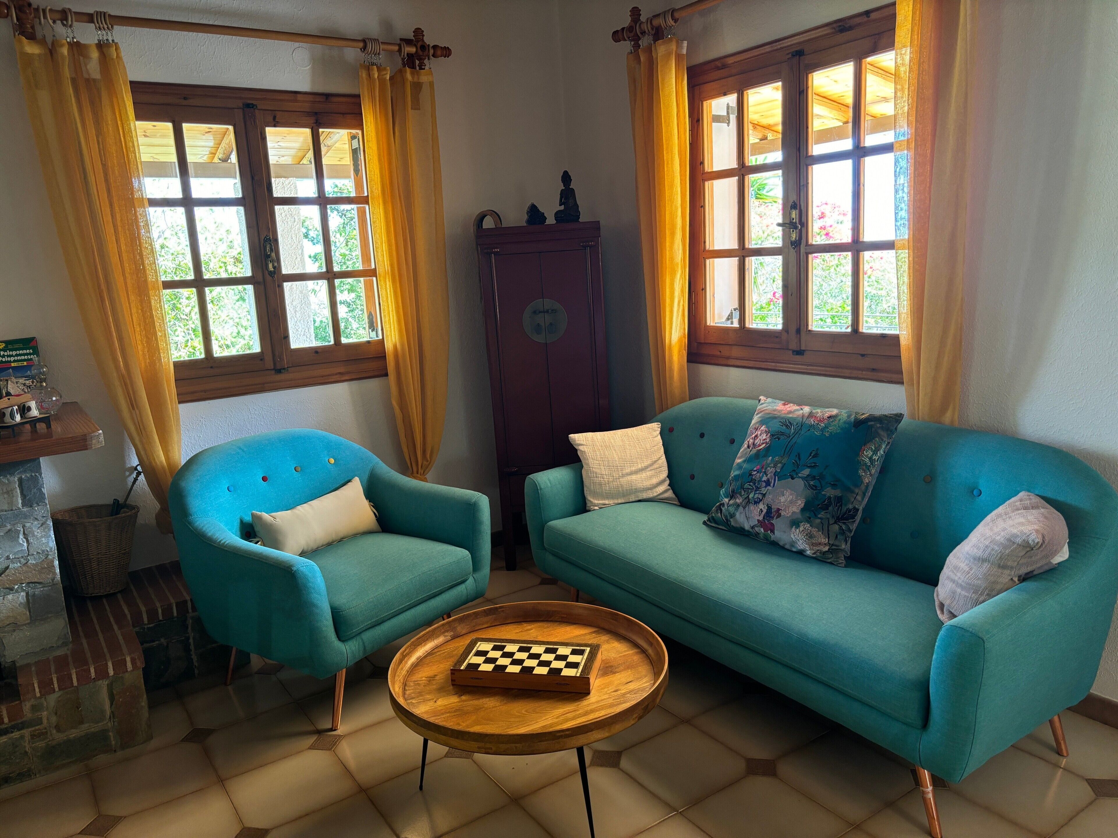 A room with a blue armchair, a teal sofa, a wooden coffee table with a chessboard, and a wooden cabinet.