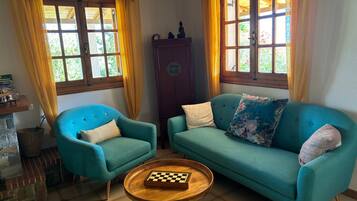 A room with a blue armchair, a teal sofa, a wooden coffee table with a chessboard, and a wooden cabinet.