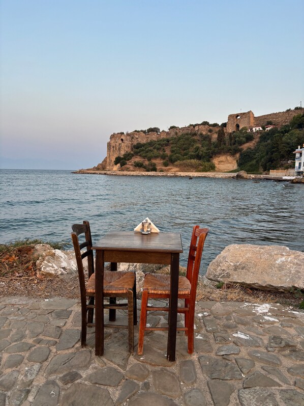 Una mesa y sillas de piedra junto al mar, con vistas a un fuerte histórico.