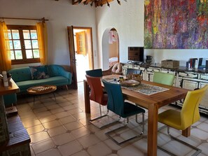 Una sala de estar con sofá, una mesa de comedor con sillas, una zona de cocina con estufa y un colorido cuadro abstracto en la pared.