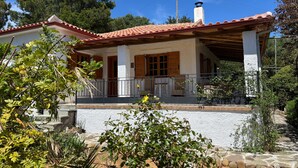 Une maison avec un toit recouvert de tuiles rouges, des murs blancs et une véranda dotée d’une balustrade.