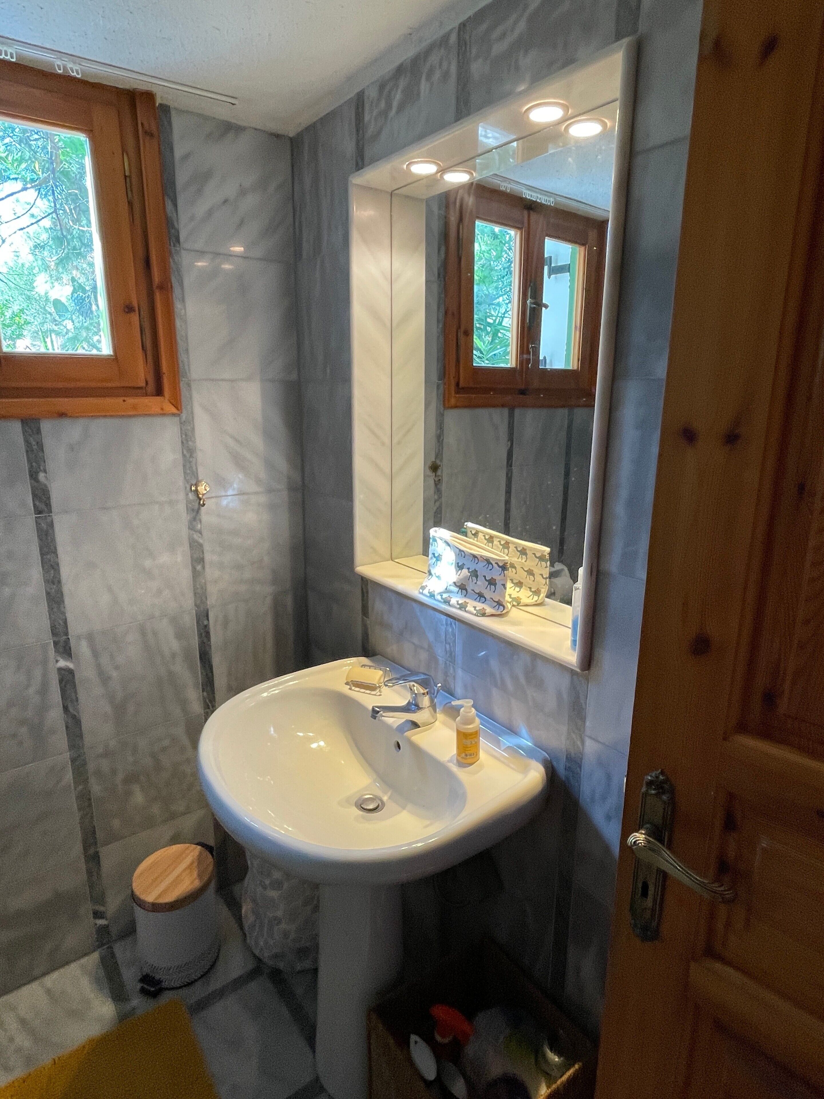 A bathroom with a marble wall, a white sink, a mirror, and a wooden door.