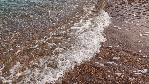 Une plage à l’eau claire, un bateau et des falaises rocheuses.