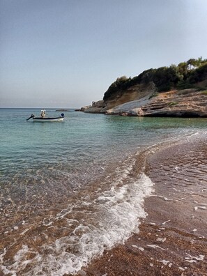 Una playa con agua cristalina, un barco y acantilados rocosos.
