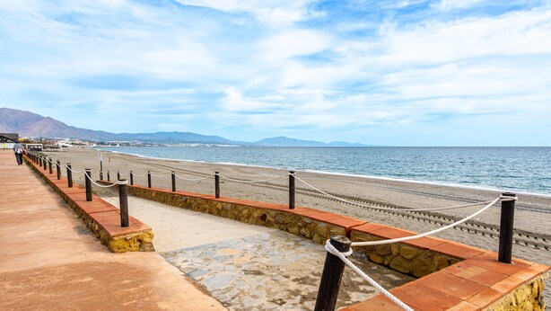 Un paseo marítimo con muro de piedra, postes de madera y barrera de cuerda.