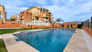 Una piscina con borde de baldosas, rodeada por una valla y edificios.