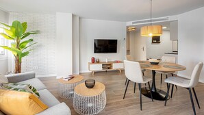 Ein modernes Wohnzimmer mit einer Couch, einem Couchtisch, einem Esstisch, Stühlen und einem Fernseher.