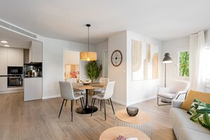 A modern kitchen with built-in appliances, a dining area with a round table and chairs, a small round table with a bowl, and a sofa with a cushion.