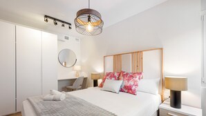 Ein ordentlich eingerichtetes Hotelzimmer mit Bett, Nachttischen, Schreibtisch, Stuhl, Kleiderschrank und einer Pendelleuchte.