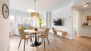 Ein modernes Wohnzimmer mit Essbereich, einem an der Wand montierten Fernseher und einem großen Fenster.