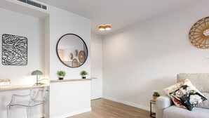 A modern living room with a clear glass chair, a wooden coffee table, a grey sofa with floral cushions, a round mirror, and wall art.