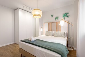 En pænt redt seng med et grønt tæppe, en sengetavlelampe og en hylder med pyngegenstande.