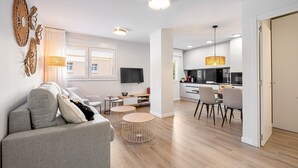 A modern living room with a grey sofa, two round tables, a TV, and a kitchen in the background.
