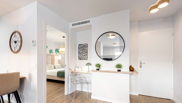 A modern interior with a wooden floor, a clear desk, a chair, a round mirror, and a door.