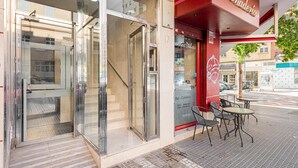A Panadería with a glass entrance, outdoor seating, and a staircase leading to an upper floor.