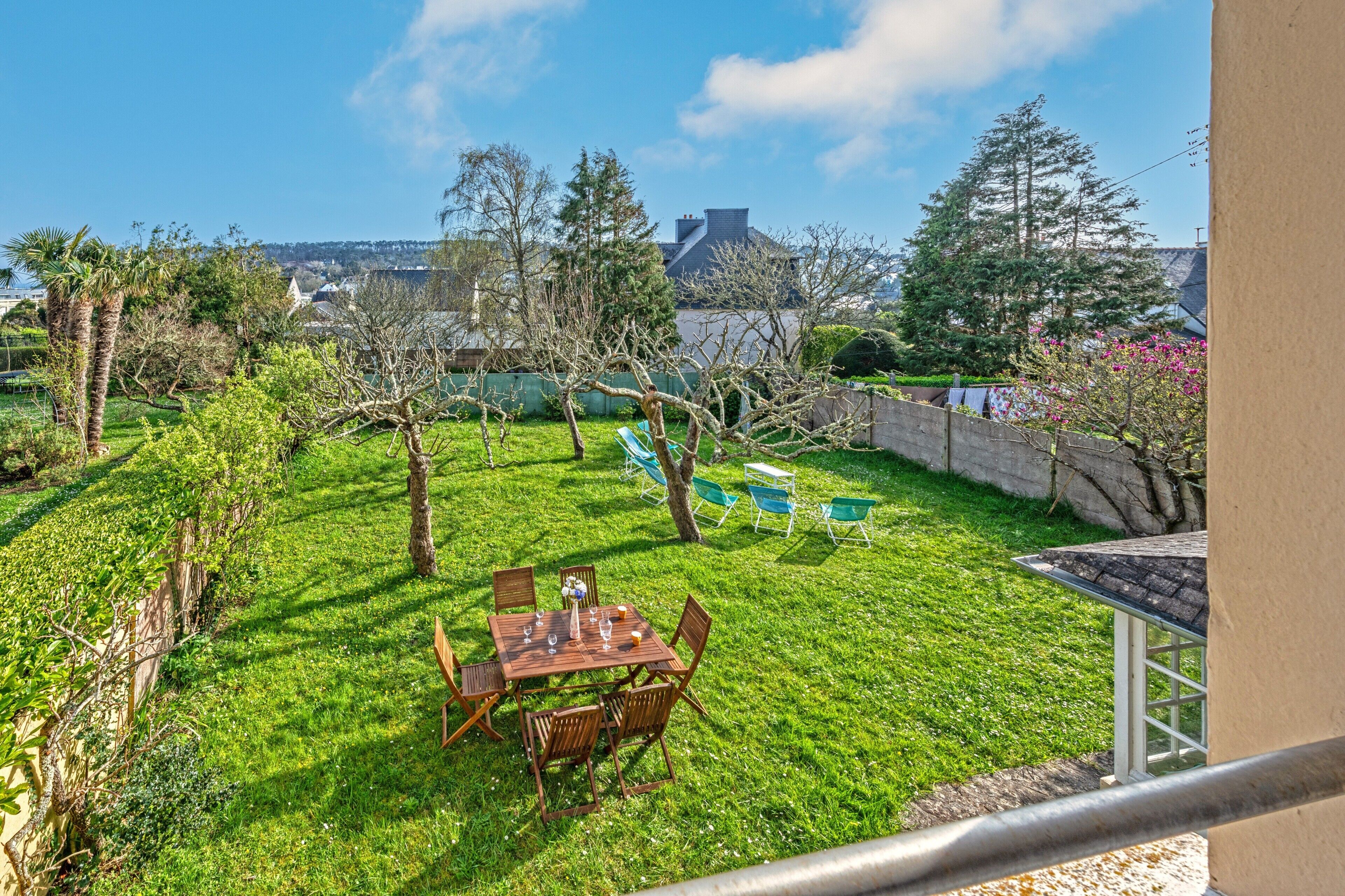 A grassy backyard with a wooden table and chairs, a small tree, and a stone wall.