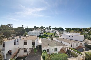 Un quartier résidentiel caractérisé par des bâtiments blancs, dont certains ont des toits plats et d’autres des toits inclinés, le tout entouré de verdure et d’arbres.