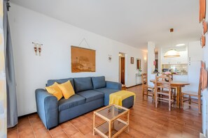 Uma sala de estar com sofá, mesa de centro de vidro e área de jantar com mesa e cadeiras de madeira.