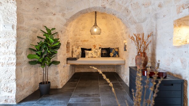A stone-walled room with a bench, a hanging light fixture, a potted plant, and a vase with dried plants. - Villa "Trulli Cinque Nicchie" with Private Terrace & Wi-Fi (Martina Franca)