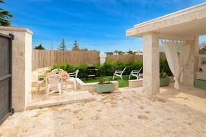 An outdoor patio area with stone flooring, white plastic chairs, a table, and a wooden fence. - Villa "Trulli Cinque Nicchie" with Private Terrace & Wi-Fi (Martina Franca)