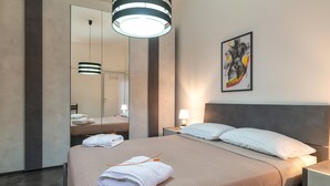 A modern hotel room with a large bed, a bedside table with a lamp, a mirror, and a painting on the wall. - Villa "Trulli Cinque Nicchie" with Private Terrace & Wi-Fi (Martina Franca)
