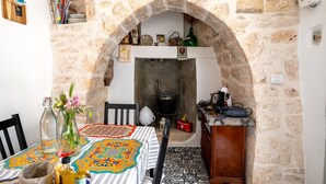 A stone archway leading to a kitchen with a tiled floor, a table with a patterned tablecloth, and various kitchen items. - Villa "Trulli Cinque Nicchie" with Private Terrace & Wi-Fi (Martina Franca)