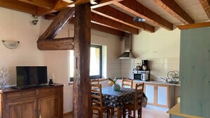 Una cocina rústica con vigas de madera, una mesa de comedor con sillas, un televisor sobre un mueble de madera y un microondas en la encimera.
