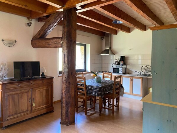 A rustic kitchen with wooden beams, a dining table with chairs, a TV on a wooden cabinet, and a microwave on the counter.
