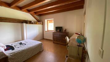A bedroom with a wooden ceiling, a bed with a patterned bedspread, a dresser, a desk with a globe, and a window with a view.