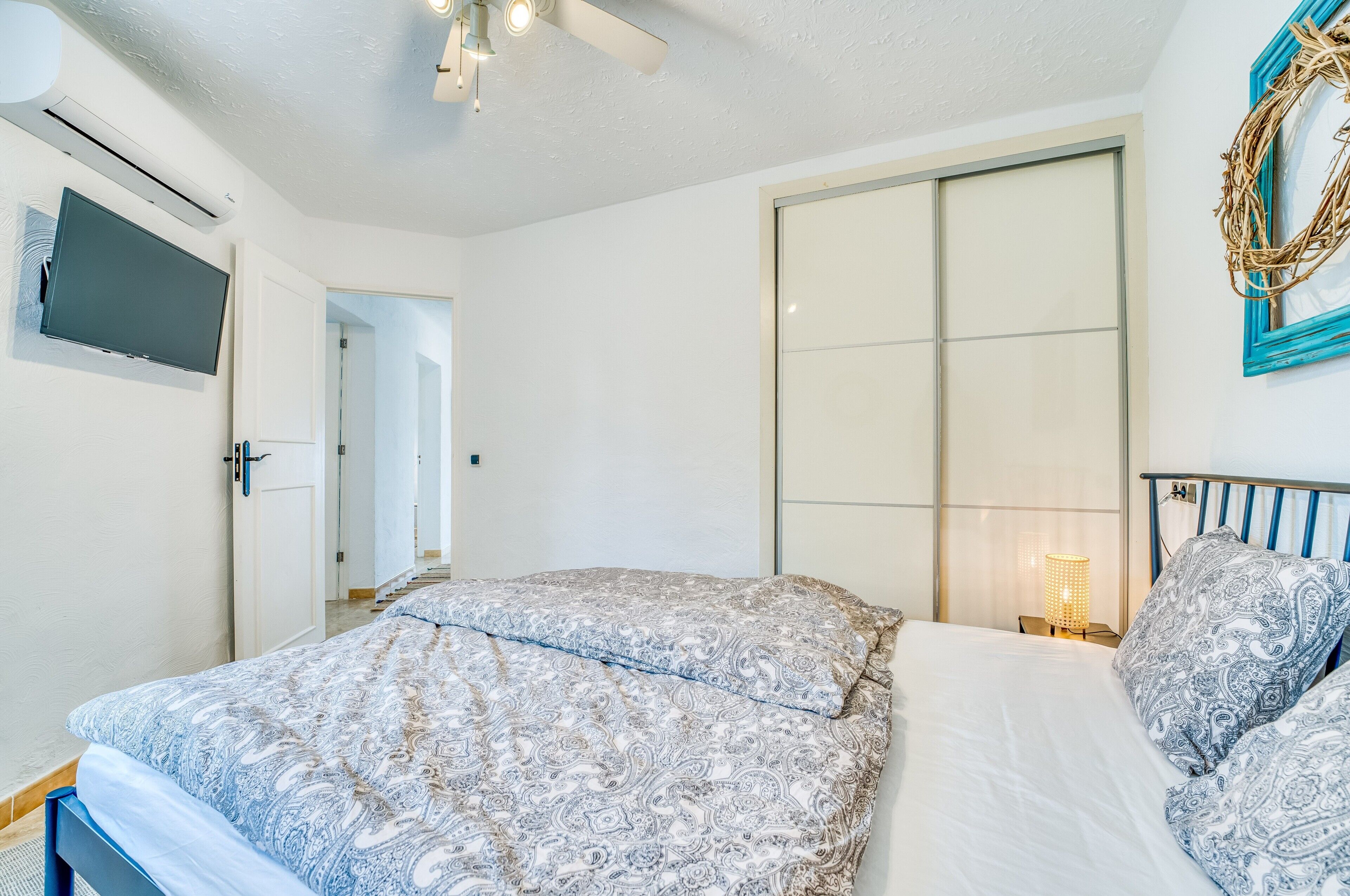 A bedroom with a bed, a TV, a wardrobe, and a nightstand with a lamp.