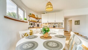 Une cuisine moderne avec des meubles blancs, une table à manger avec des sets de table et un luminaire suspendu.