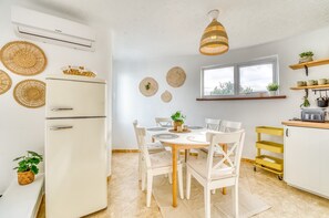 Ett modernt kök med ett vitt kylskåp, ett matbord med stolar, en hängande lampa och ett fönster med utsikt.