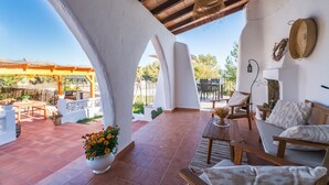 Une terrasse couverte, aménagée avec du mobilier d’extérieur, une colonne blanche et un luminaire suspendu.