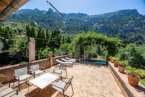 Une terrasse avec des sièges extérieurs et une piscine, le tout entouré de verdure et de montagnes.