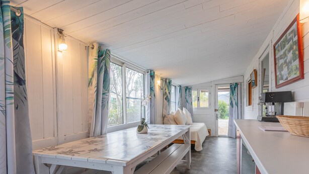 Een gezellige kamer met een witte houten bank, een bed met kussens, een tafel met een lamp en een aan de muur hangend fotokader.