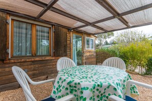Une cabane en bois dotée d’un patio couvert, d’une table avec des chaises et offrant une vue sur la verdure.
