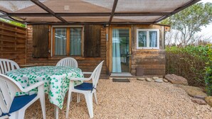 Een houten hut met een overdekte veranda, een tafel met stoelen en een grindpad.