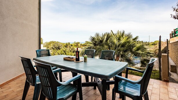 A patio with a table and chairs, surrounded by greenery and a clear sky.