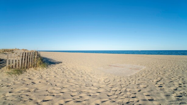 Una spiaggia sabbiosa con impronte, una recinzione in legno e l'oceano sullo sfondo.