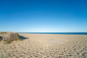 A sandy beach with footprints, a wooden fence, and the ocean in the background.