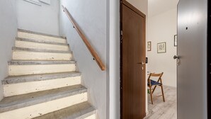 Una scala con ringhiera in legno, una porta in legno e una sedia in un corridoio con pavimento chiaro.