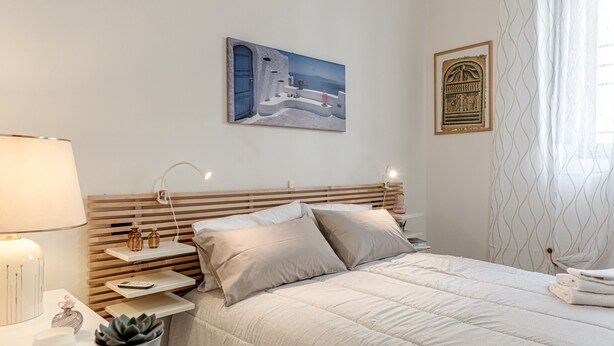 Una camera d'albergo ordinata con un letto, comodini, una lampada, una pianta in vaso e opere d'arte alle pareti.