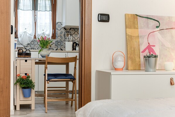 Une pièce de taille modeste, comprenant un bureau en bois, une chaise, un lit, une petite kitchenette et un tableau accroché au mur.