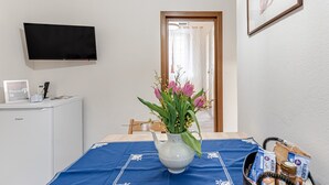 Una camera d'albergo con un letto, una televisione a parete, un piccolo mobile, un vaso con fiori e un cesto di snack.