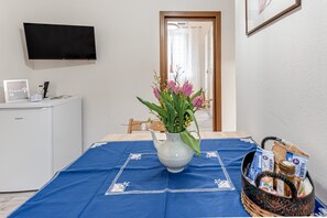 A hotel room with a bed, a TV mounted on the wall, a small cabinet, a vase with flowers, and a basket with snacks.